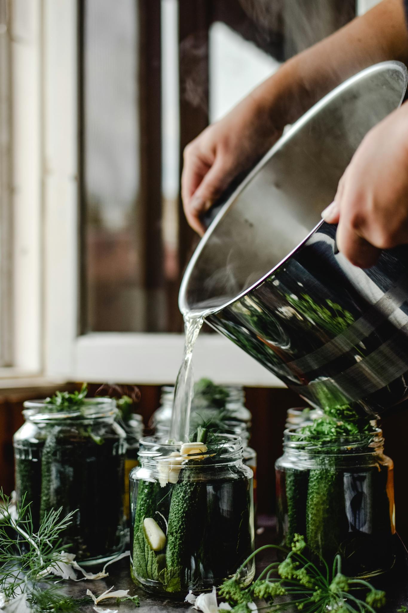 Fresh cucumbers being pickled in glass jars with herbs for homemade preservation.